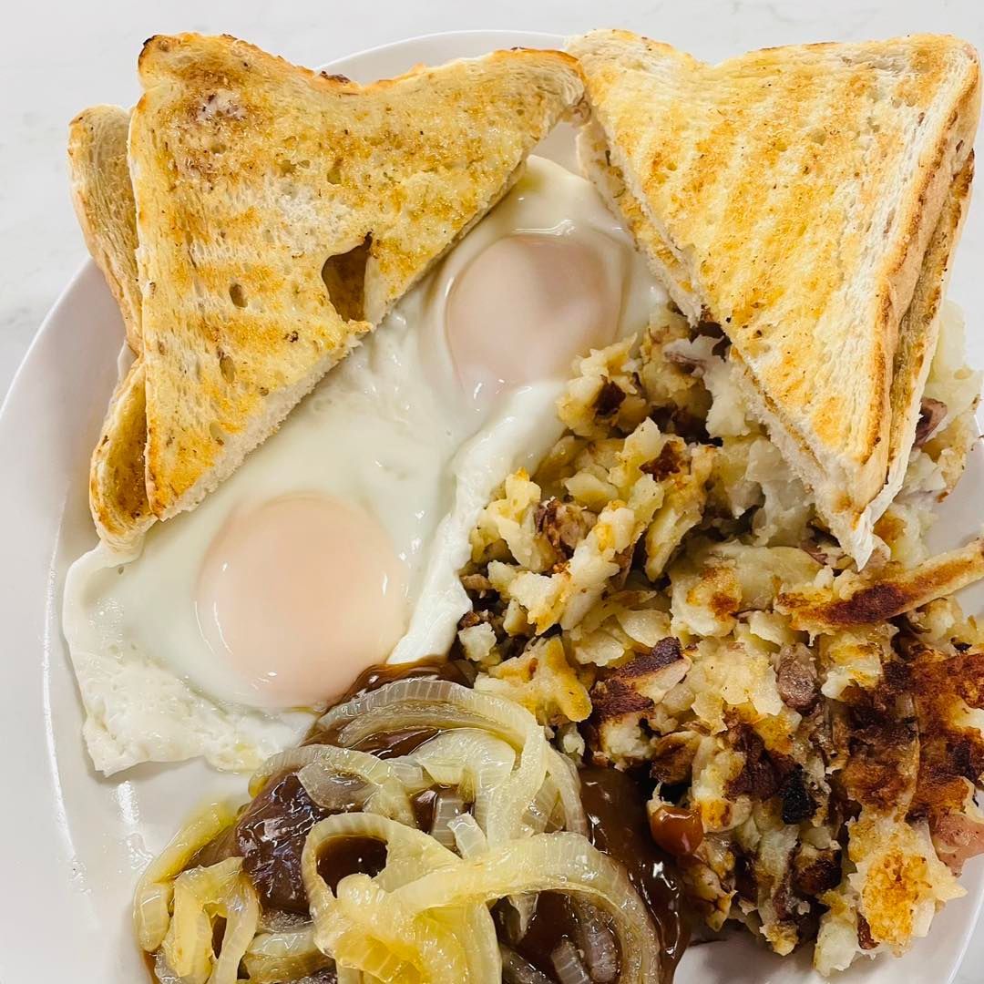 Toast triangles, two sunny-side eggs, scrambled potatoes, and onion rings on a white plate