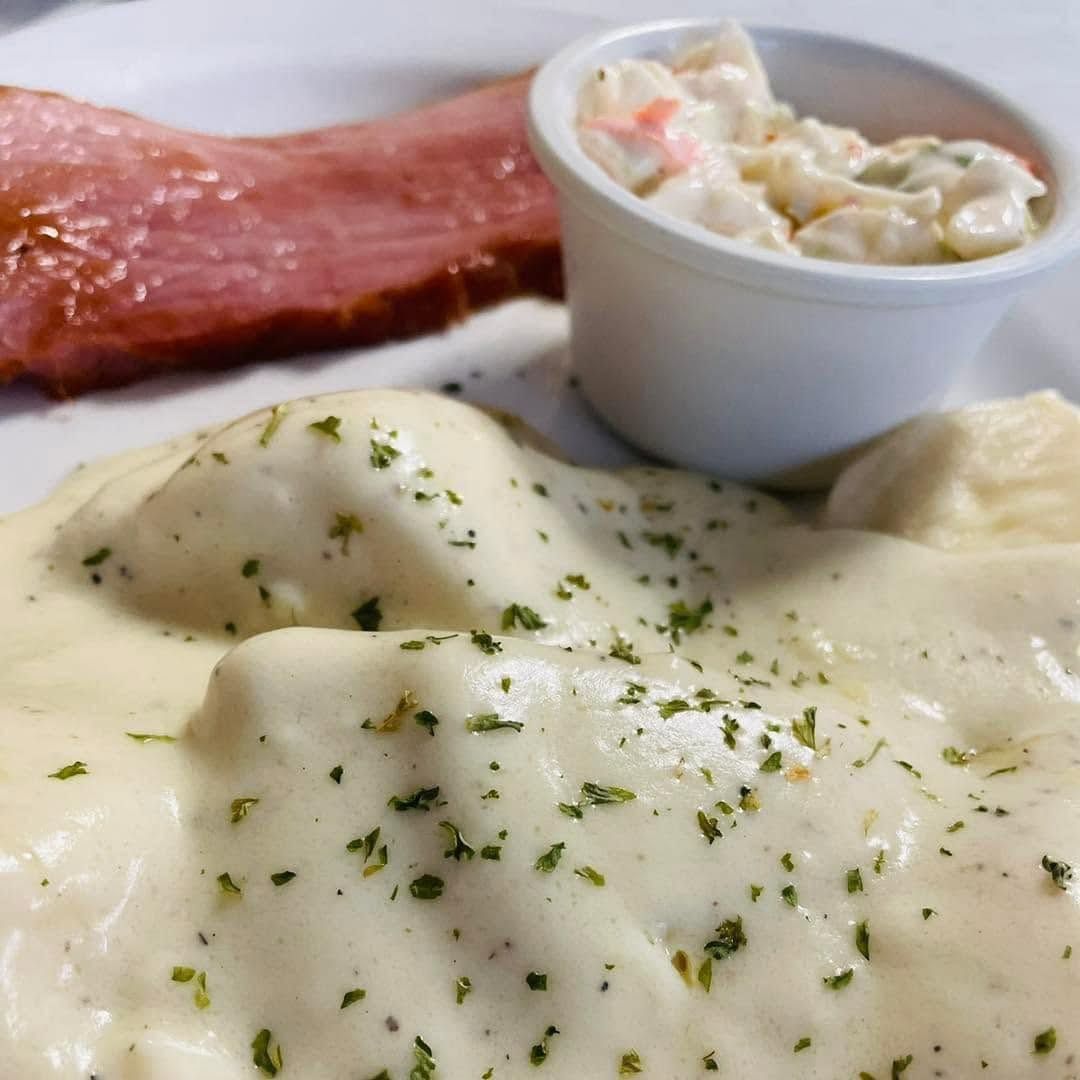 Plate of mashed potatoes with gravy, bacon strips, and a small cup of coleslaw with parsley garnish