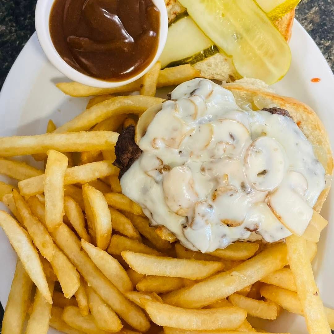 French fries and a mushroom burger topped with creamy sauce, with pickle spears and gravy on the side.