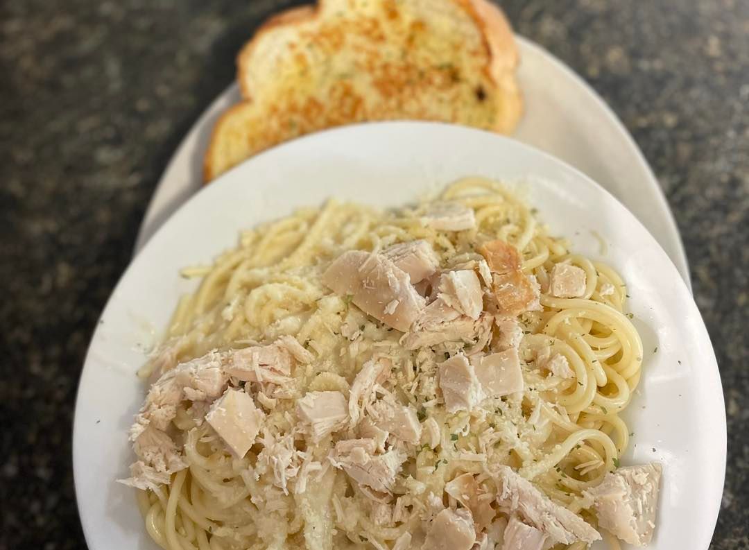 Chicken pasta Alfredo in a white bowl with garlic bread on a plate behind it