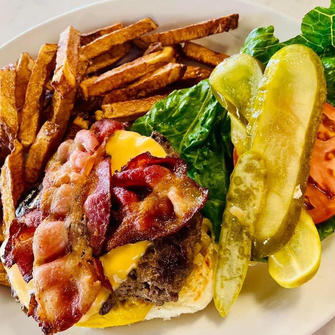 Bacon cheeseburger with fries and pickles on a white plate