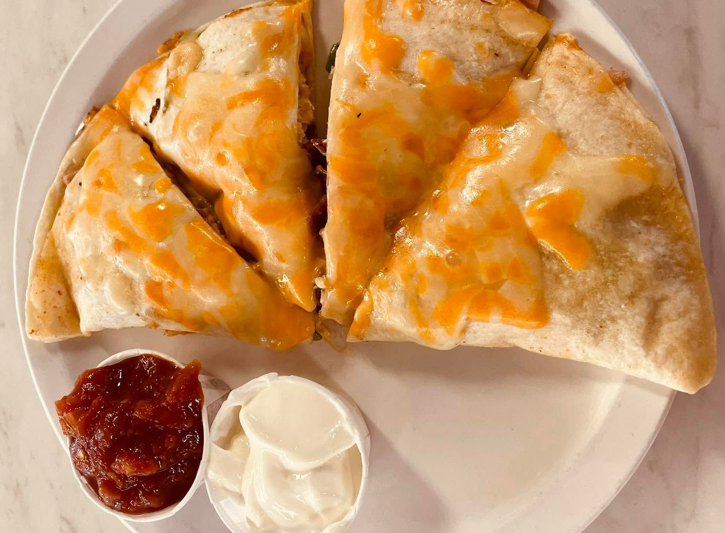 Cheesy quesadilla slices on a plate with salsa and sour cream on the side
