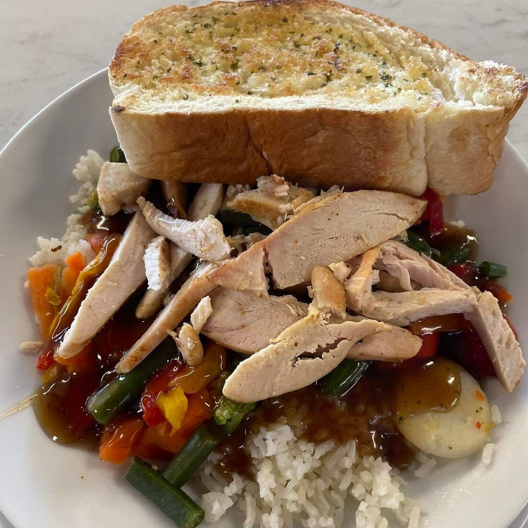 Sliced turkey over rice with vegetables and gravy, topped with a slice of garlic bread.