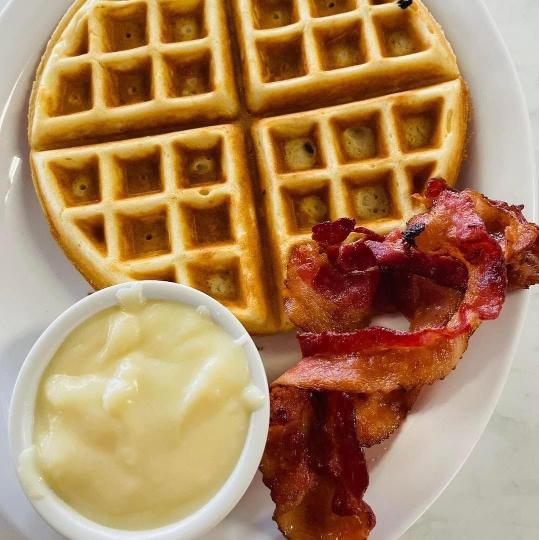 Waffle with bacon and a cup of butter or cream on a white plate
