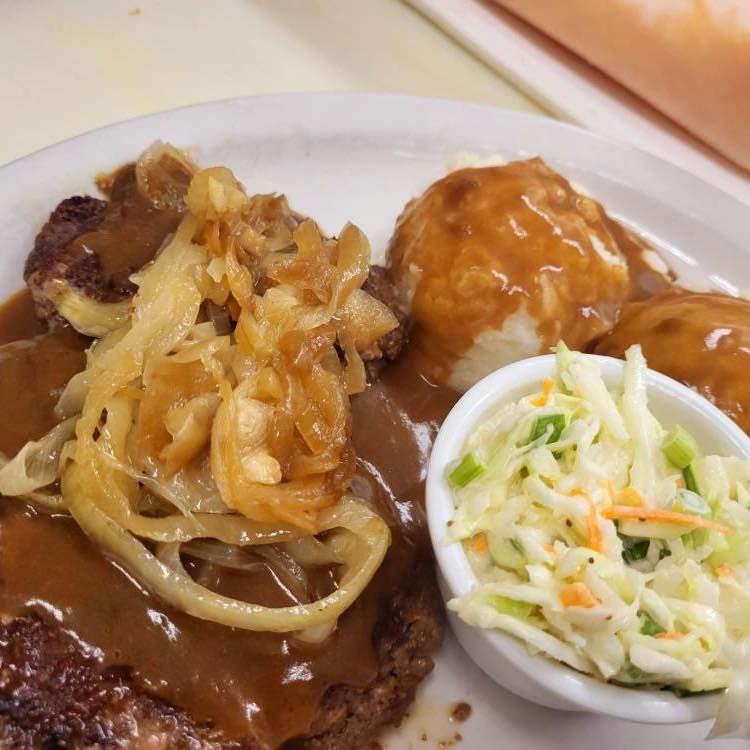 Plated meat with gravy, onions, mashed potatoes, and coleslaw on a white dish