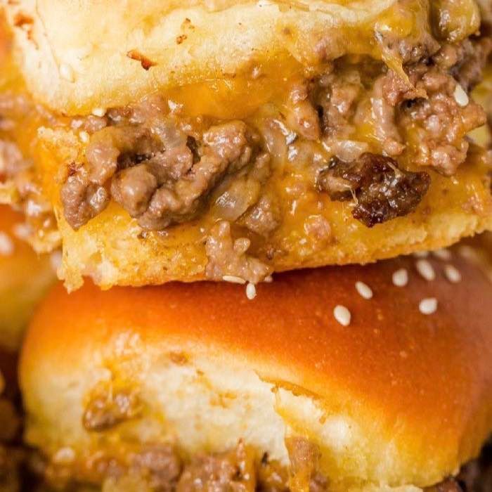 Close-up of stacked beef sliders on sesame seed buns with melted cheese and saucy filling