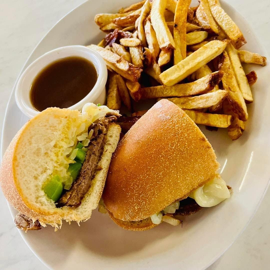 Sandwich and fries on a white plate with a cup of brown dipping sauce