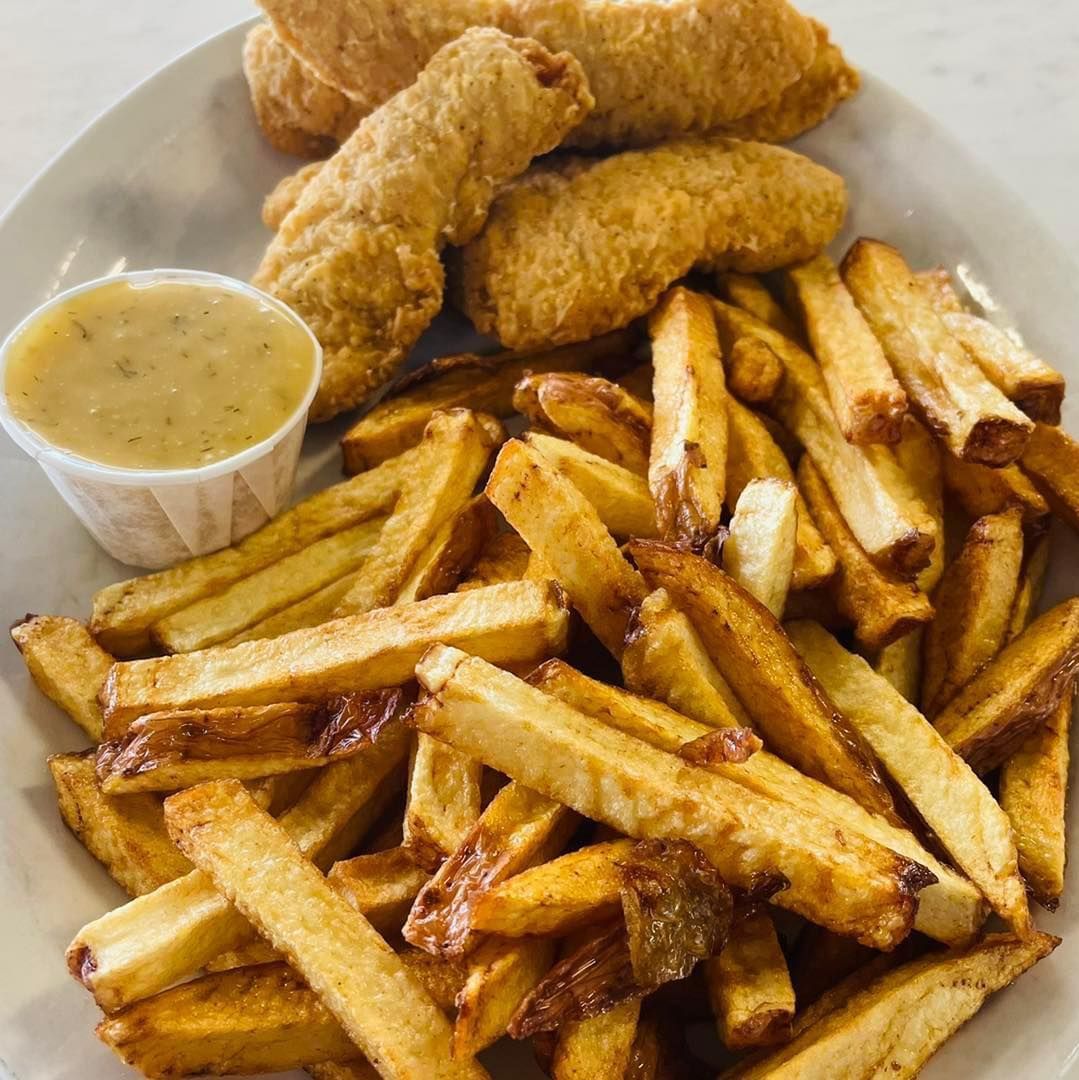 Fried chicken tenders with golden fries and a cup of dipping sauce on a plate