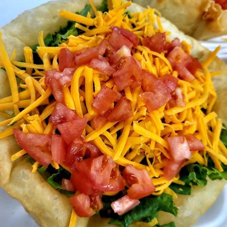 Fried flatbread topped with shredded cheddar, diced tomatoes, and leafy greens