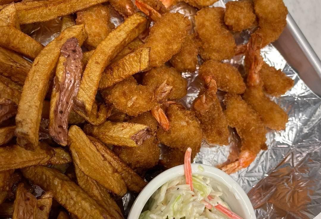 Tray of seasoned fried potato wedges with a small cup of coleslaw on foil-lined paper