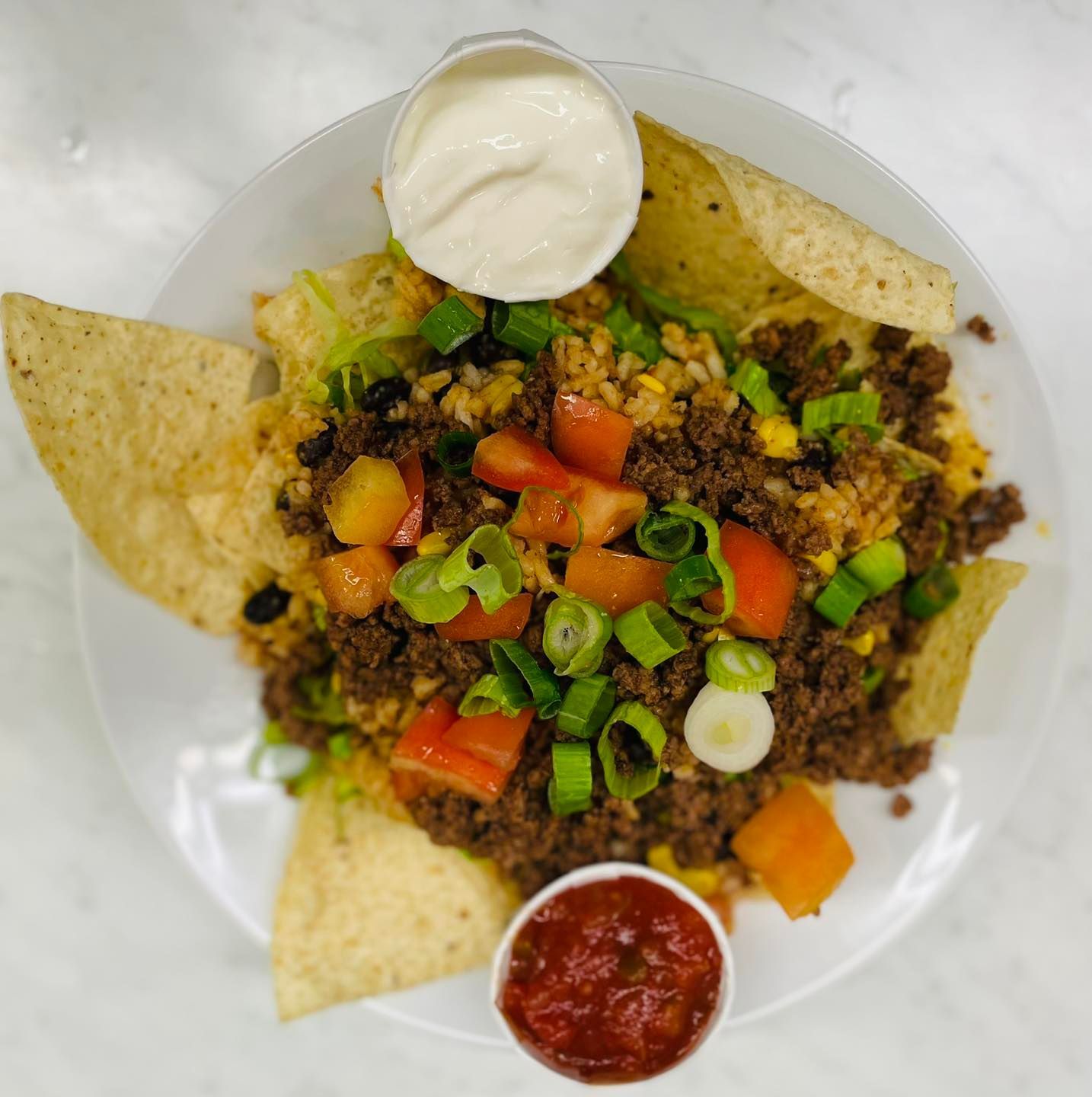 Nachos with seasoned meat, tomatoes, green onions, sour cream, and salsa on a white plate