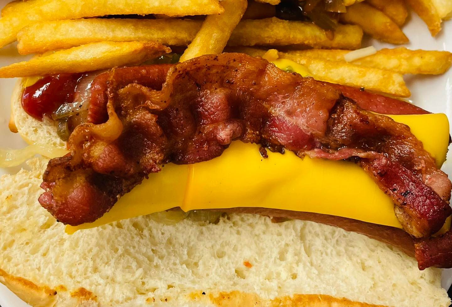 Close-up of a cheeseburger with bacon and fries on top, showing melted yellow cheese and a bun.