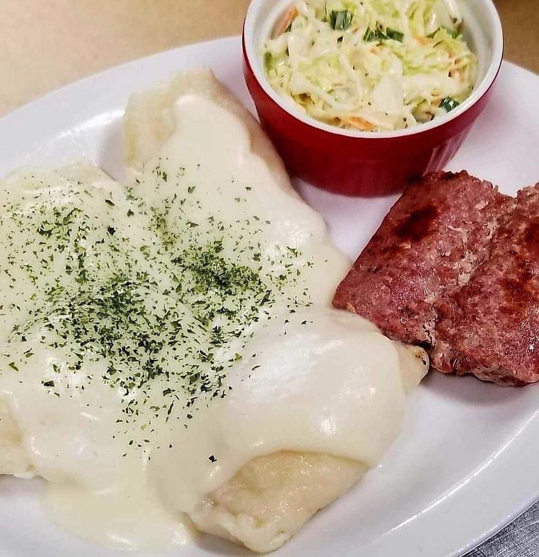 Plate of creamy white sauce over potatoes, with a red cup of coleslaw and a slice of corned beef