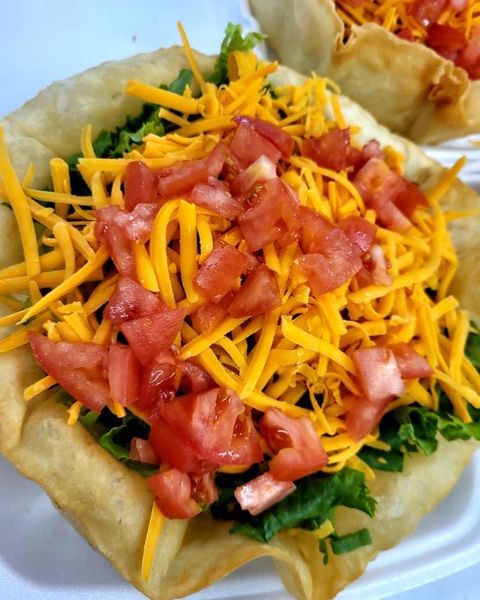 Taco shell topped with lettuce, shredded cheese, and diced tomatoes on a white plate