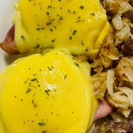 Two eggs Benedict with bright yellow hollandaise on a plate, garnished with herbs
