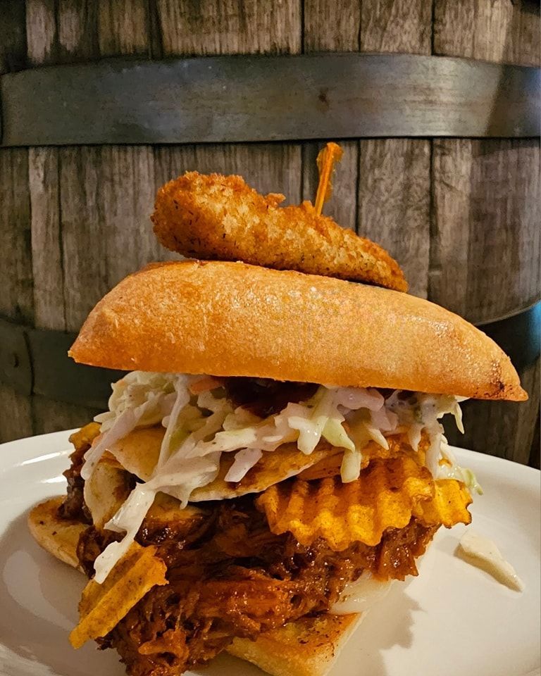 Pulled pork sandwich with coleslaw, waffle fries, and a fried appetizer on a white plate