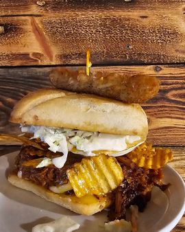 A sandwich with crispy fries and a fried pickle on a plate over a wooden table.