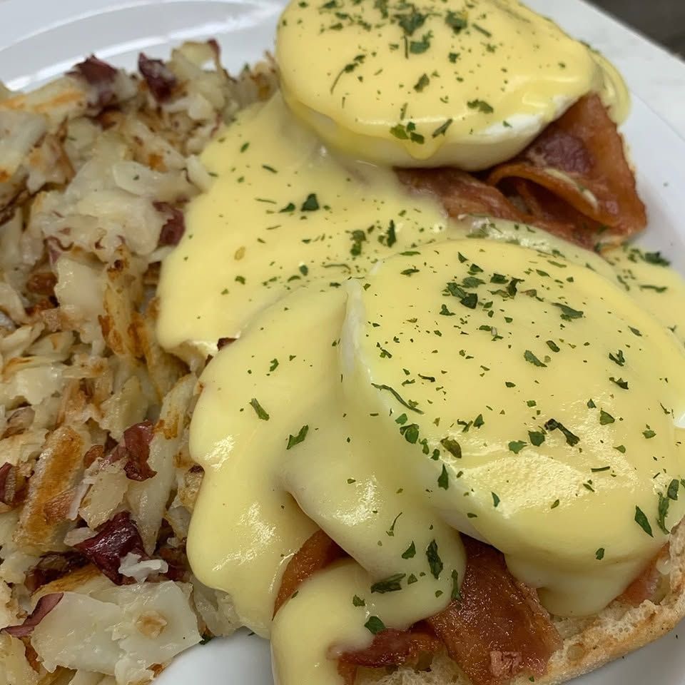 Eggs Benedict with hollandaise sauce, parsley, and crispy hash browns on a white plate