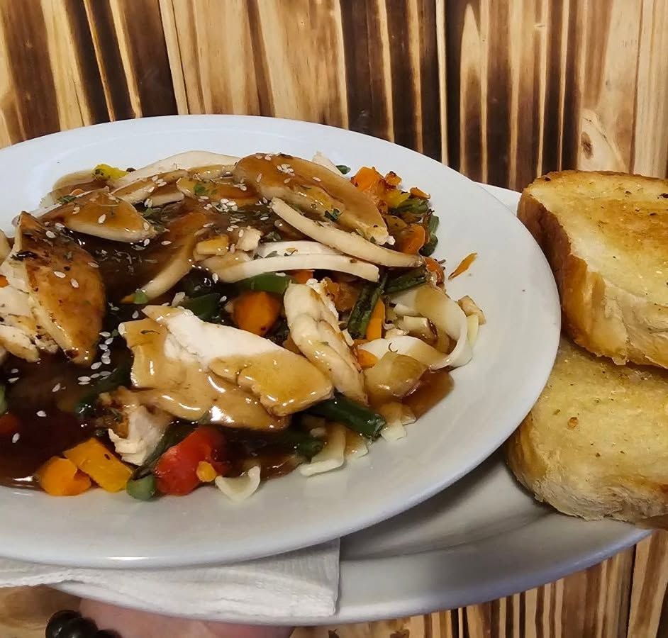 Plate of chicken and vegetables in brown sauce beside two slices of toasted bread on a table