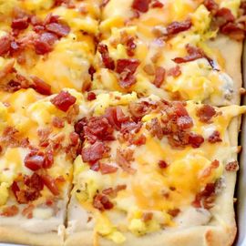 Cheesy breakfast pizza with scrambled eggs and bacon on a golden crust