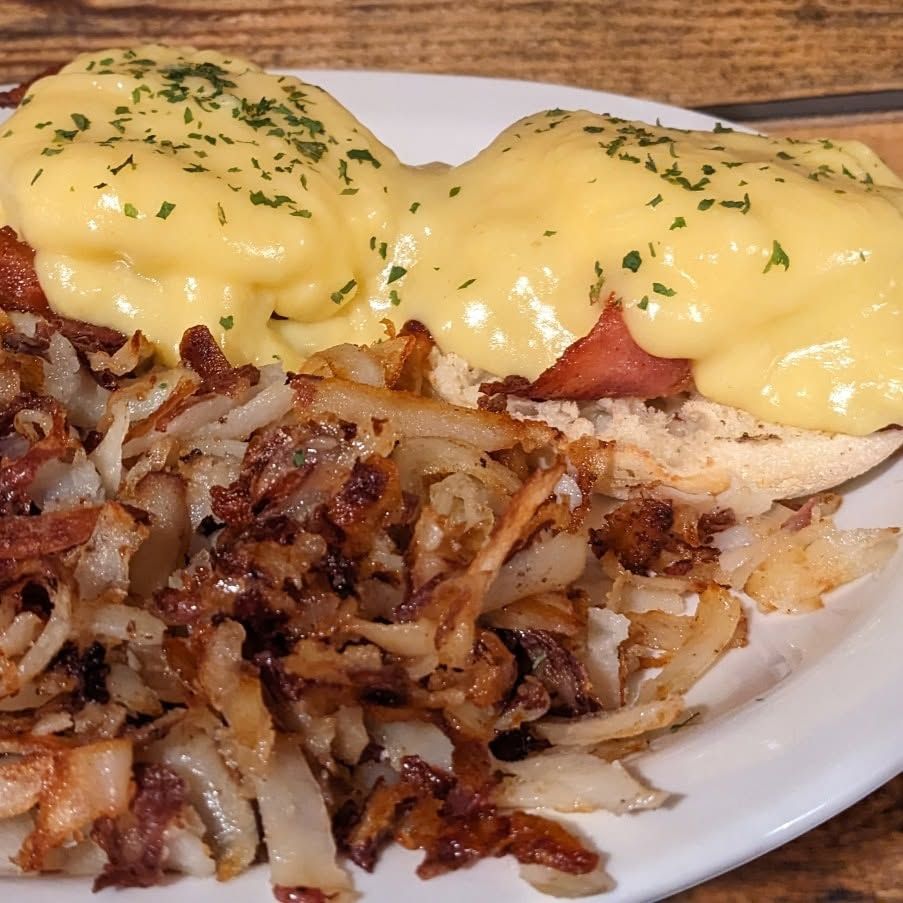Breakfast plate with eggs Benedict topped with hollandaise and parsley, served with crispy hash browns.