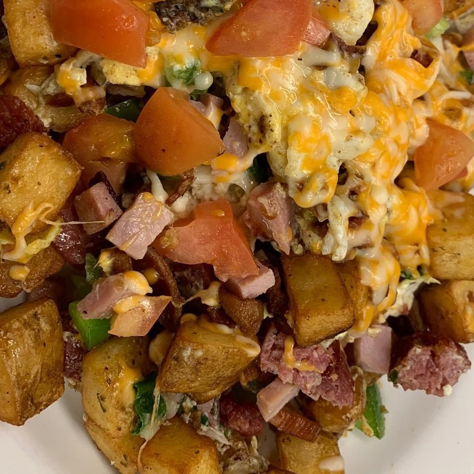 Cheesy loaded potato skillet with diced tomatoes, ham, peppers, and browned potatoes on a white plate
