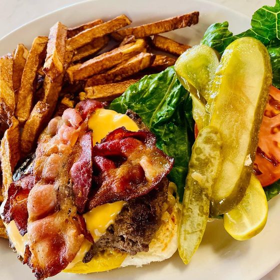 Bacon cheeseburger with fries and pickle slices on a white plate