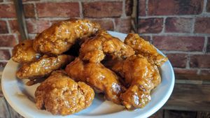 Plate of glazed fried chicken pieces on a white plate in front of a brick wall