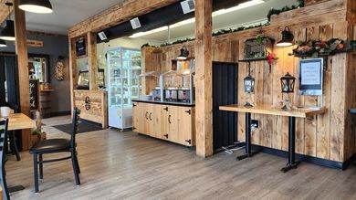 Rustic cafe interior with wooden counters, brick walls, hanging lights, and a high table by the window.
