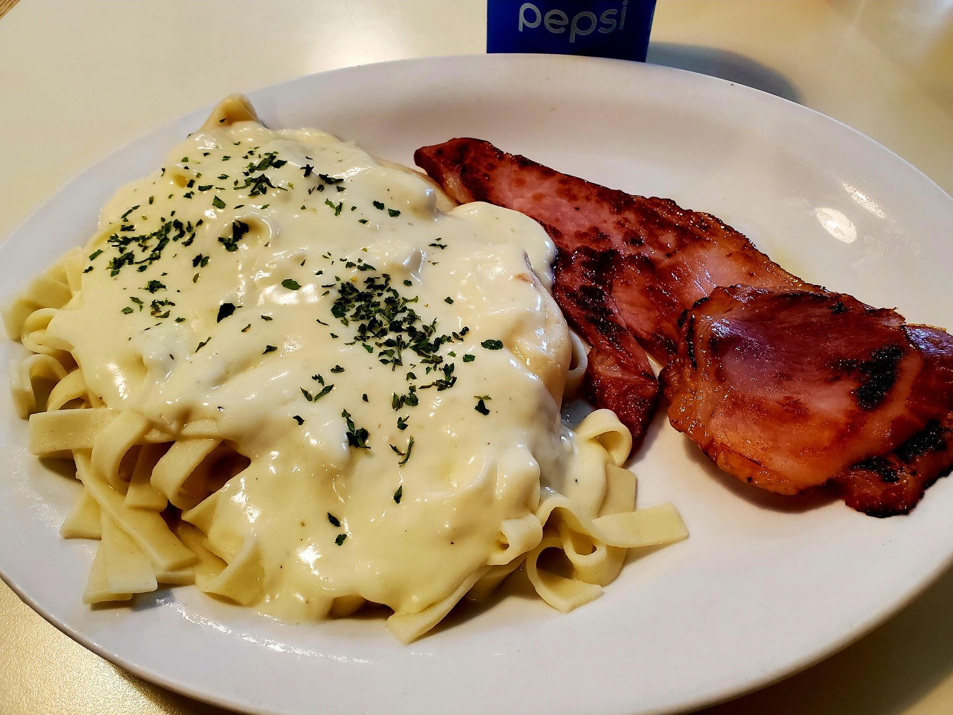Pasta with creamy white sauce and herbs beside two strips of bacon on a white plate.
