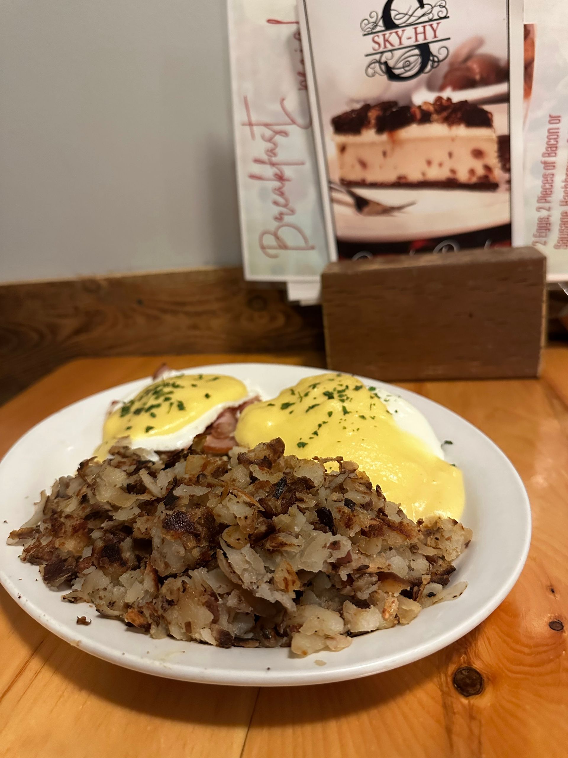 Plate of eggs Benedict with hash browns on a wooden table, with a menu stand in the background