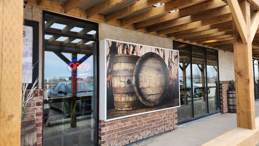 Covered outdoor storefront with wooden beams and a large barrel mural beside glass doors.