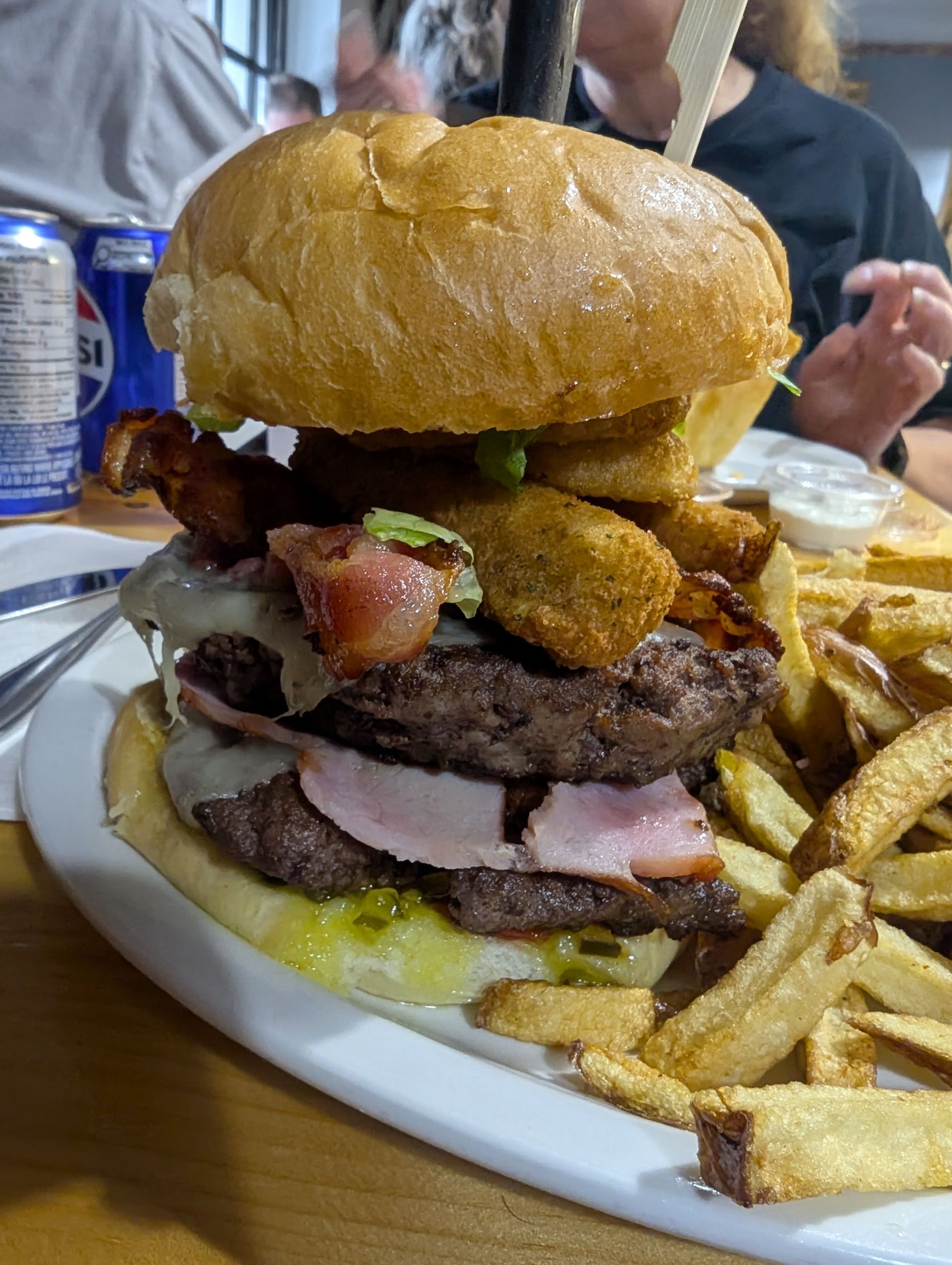 Stacked burger with fries on a white plate at a restaurant table