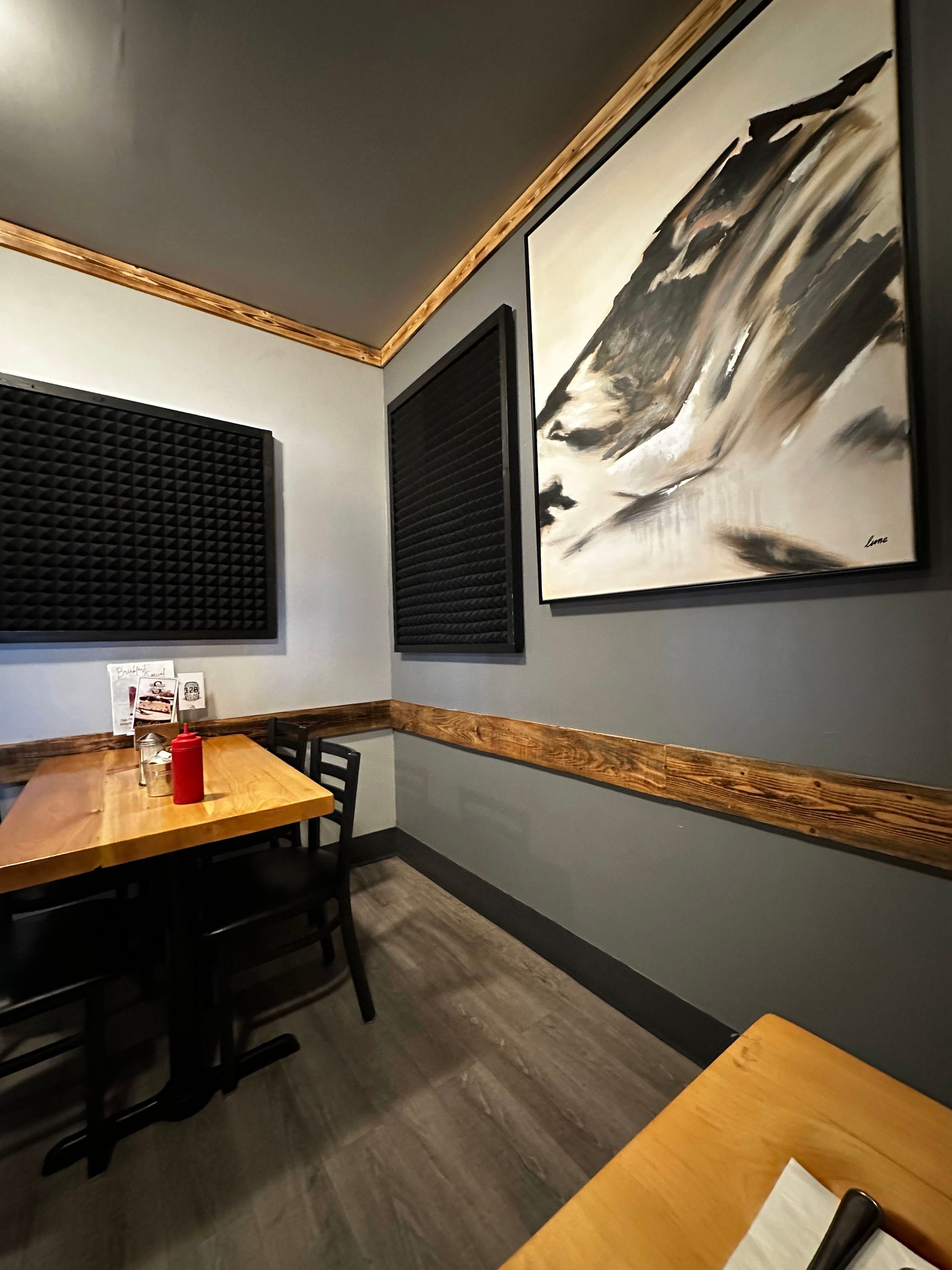 Small modern booth with black sound panels, wood tables, and abstract wall art in a cozy room.