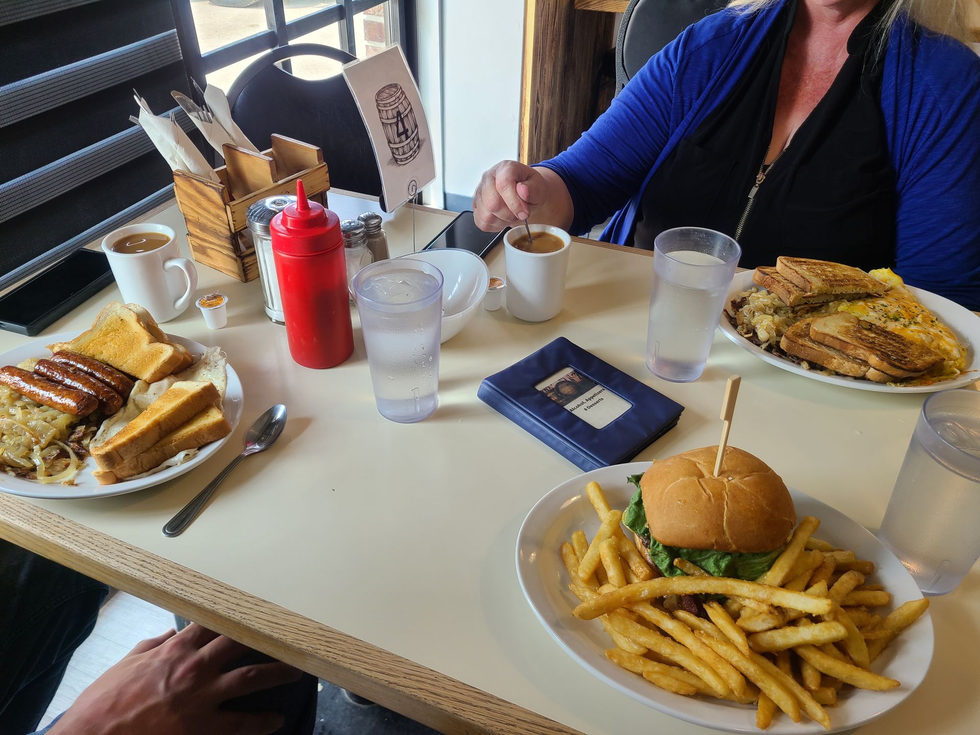 Restaurant table with burgers, fries, sandwiches, drinks, and a ketchup bottle