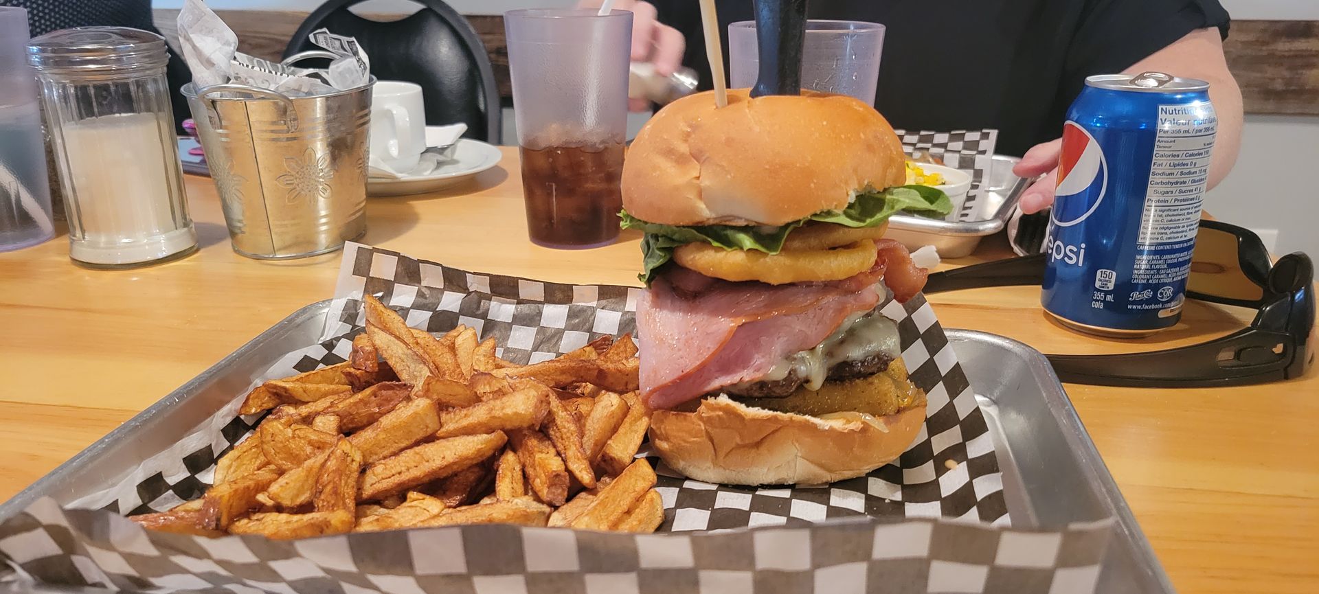 Burger and fries on a checkered tray with a soda can on a restaurant table.