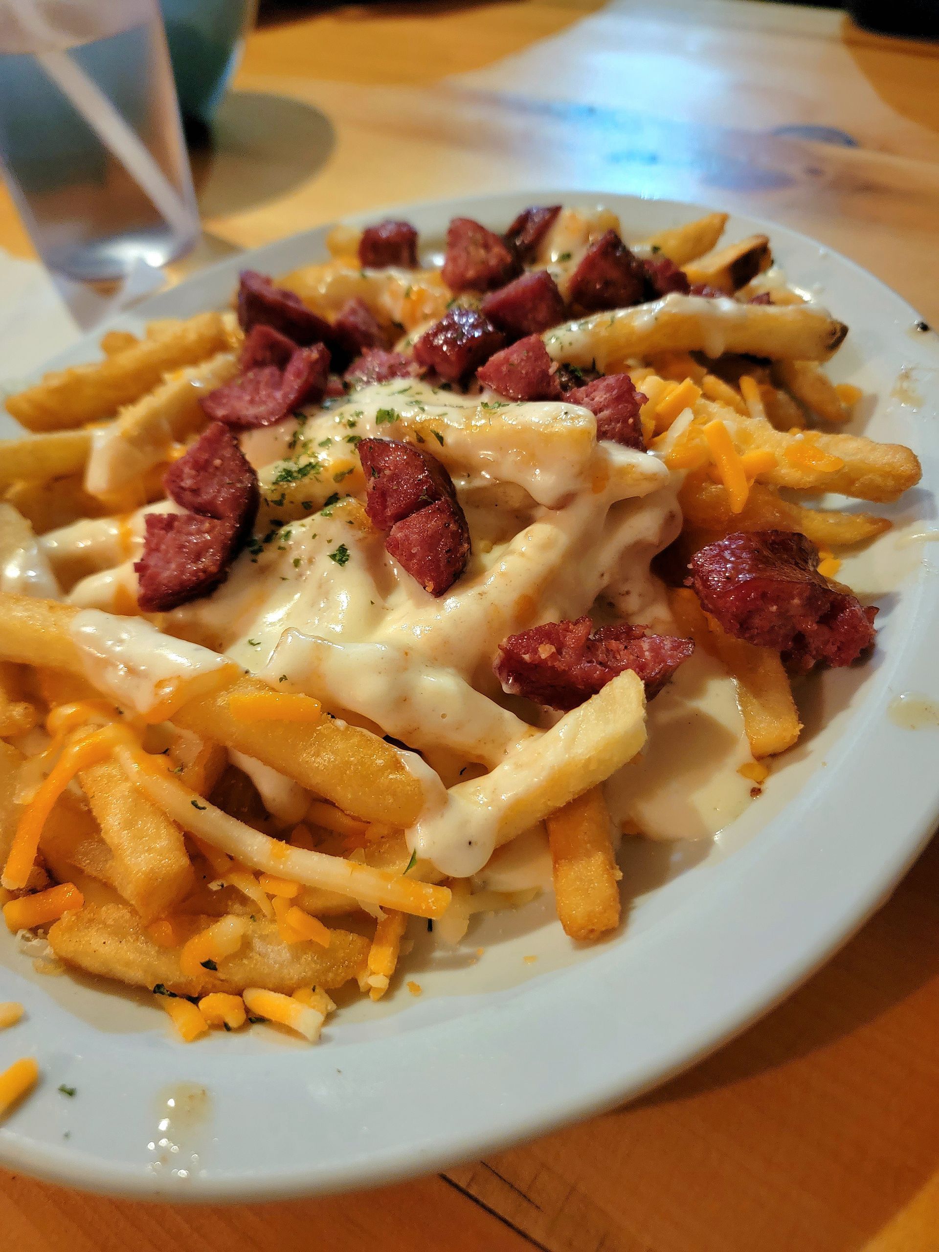 Plate of fries topped with melted cheese and diced meat on a white dish
