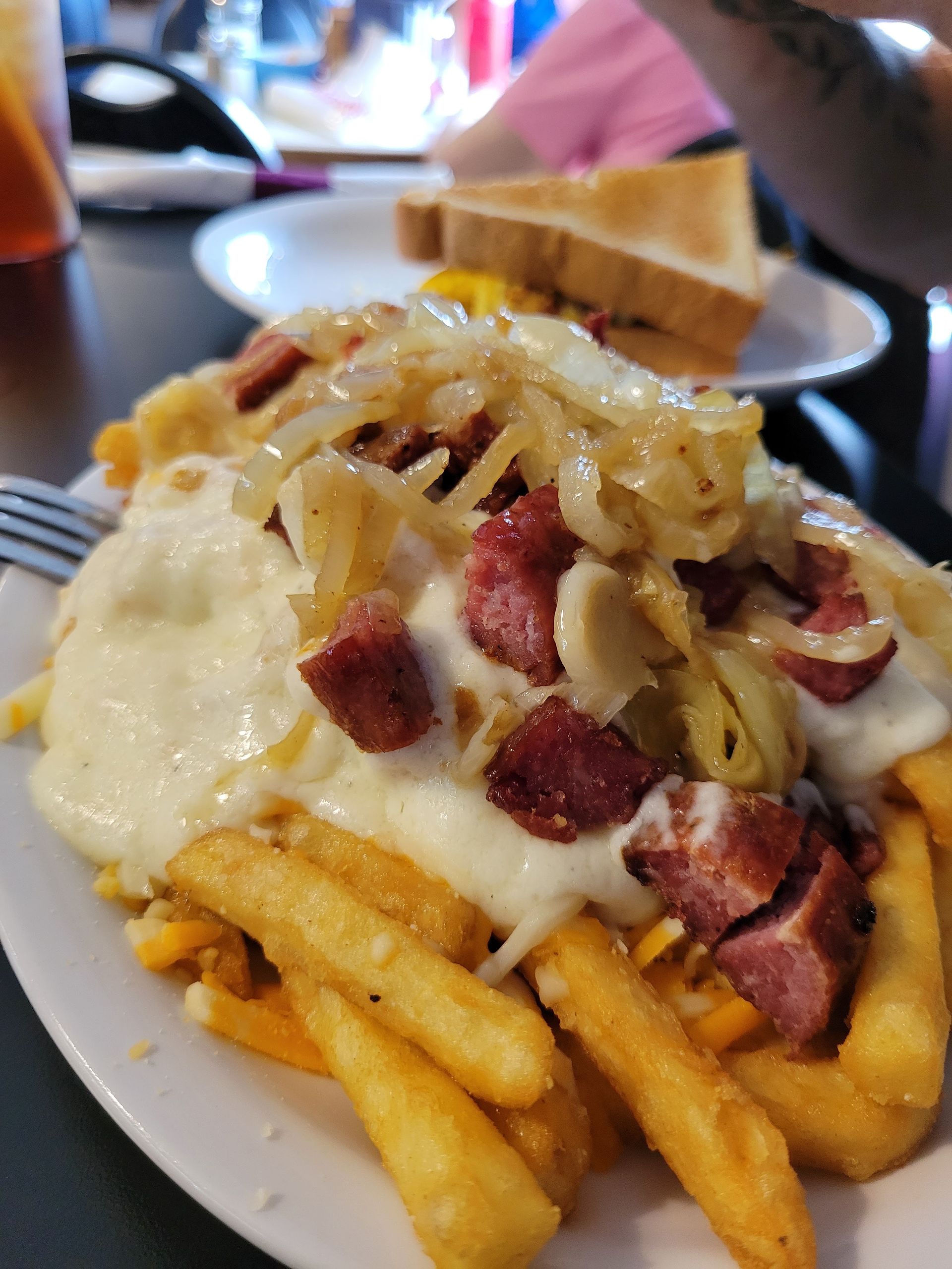 Fries topped with sausage, onions, and melted cheese on a white plate at a restaurant table