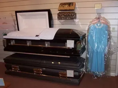 Funeral home display: open casket, stacked closed caskets, blue dress in plastic, wooden wall.
