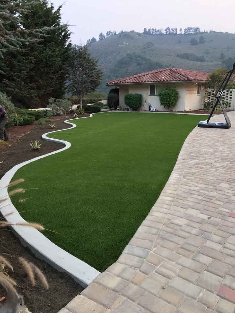 A brick walkway leading to a large lawn with a house in the background.