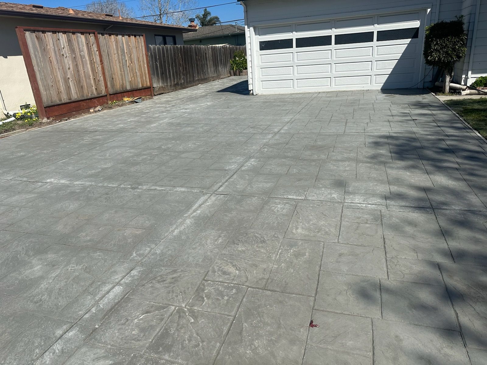 A concrete driveway leading to a garage with a wooden fence in the background.