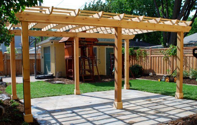 A wooden pergola is in the backyard of a house.