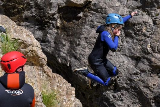 Dos escaladors amb cascos blau i vermell enfilant-se per una paret rocosa.