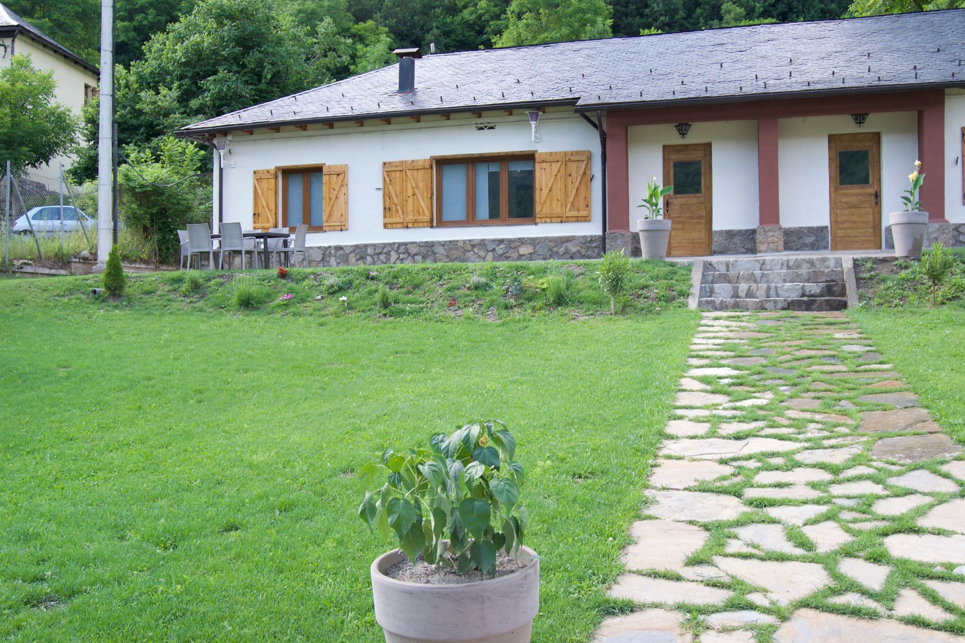 Casa petita amb un camí de pedra, porticons de fusta i una gespa verda en un entorn boscós