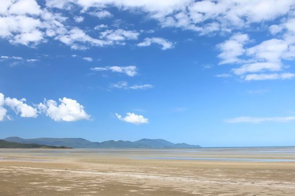 A Beach With Mountains in the Background and a Blue Sky With Clouds — Coastal Arborist Services in Cannonvale, QLD