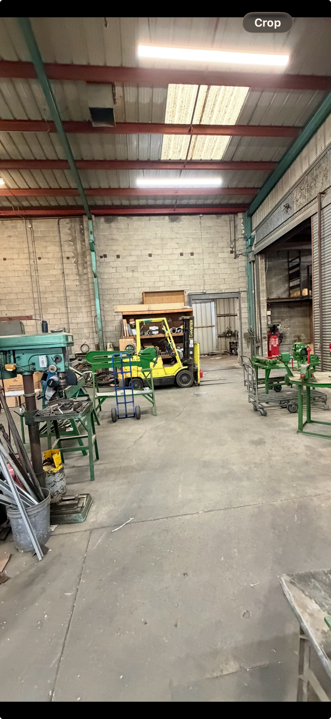 Inside a workshop, a green forklift stands amid metalworking equipment, illuminated by overhead lights.