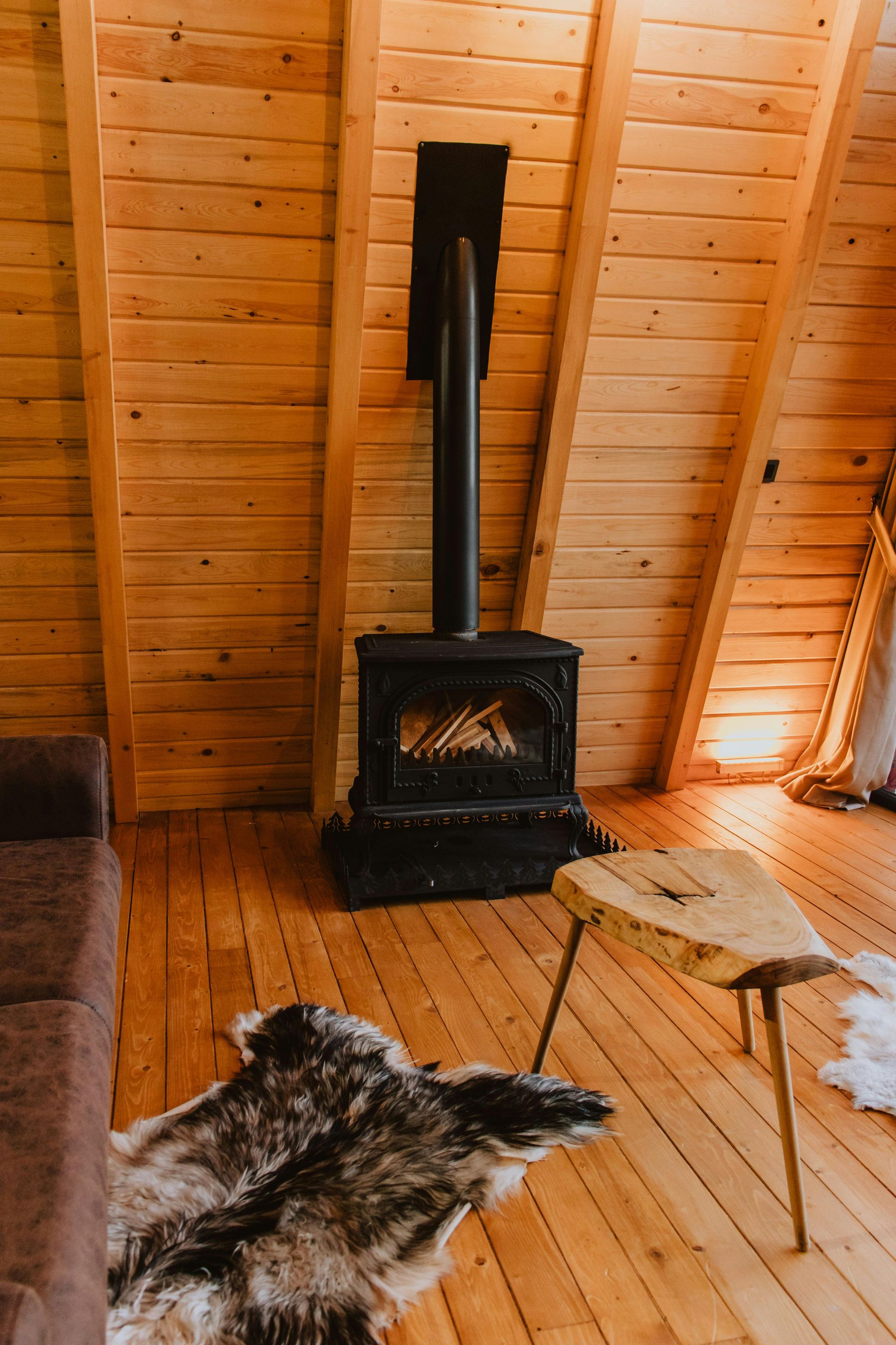 Cozy wooden cabin interior with a fireplace, rustic coffee table, and animal skin rug on the floor.