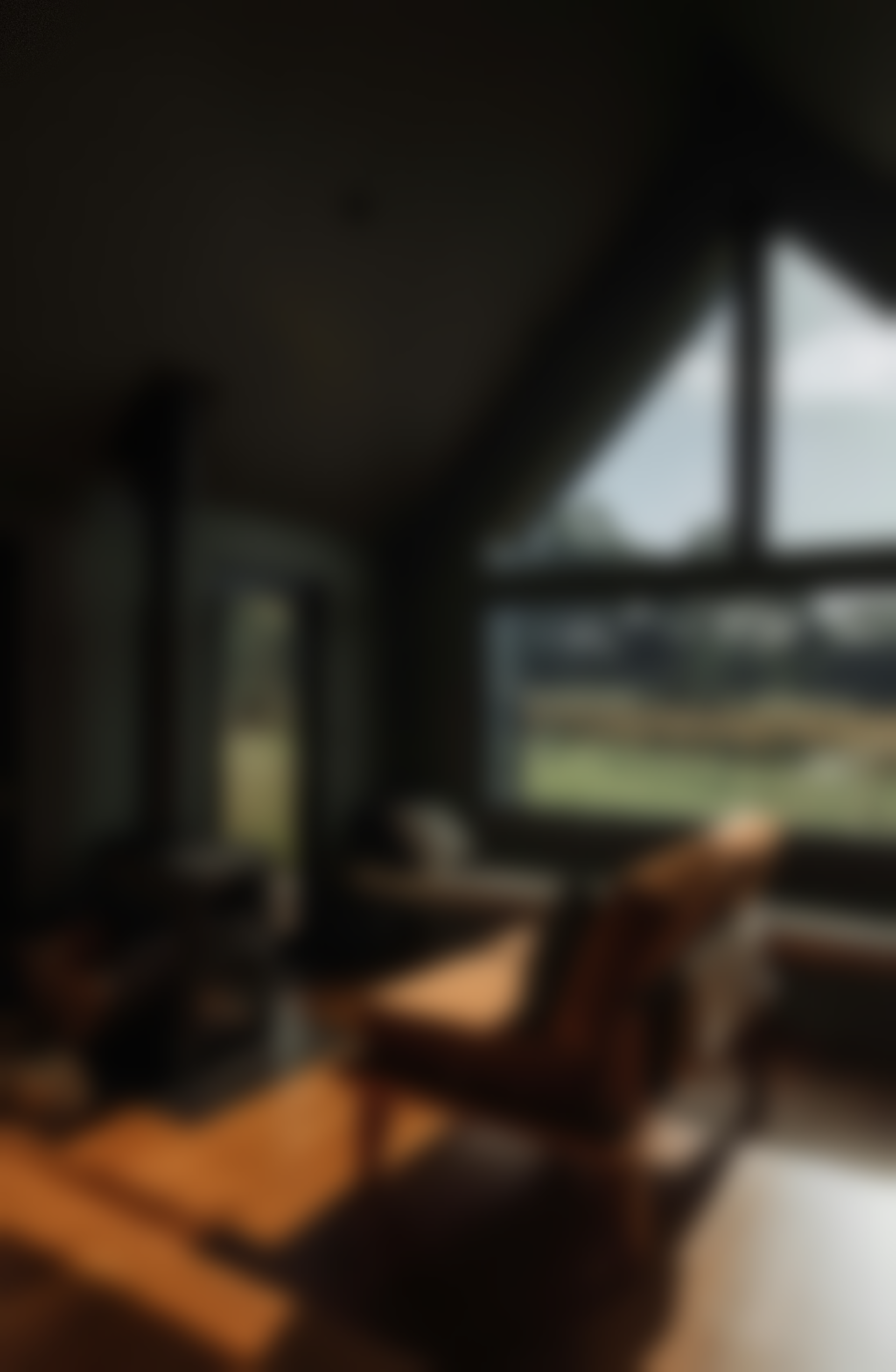 Blurred interior shot of a room with a large window. A chair and sunlight are visible.
