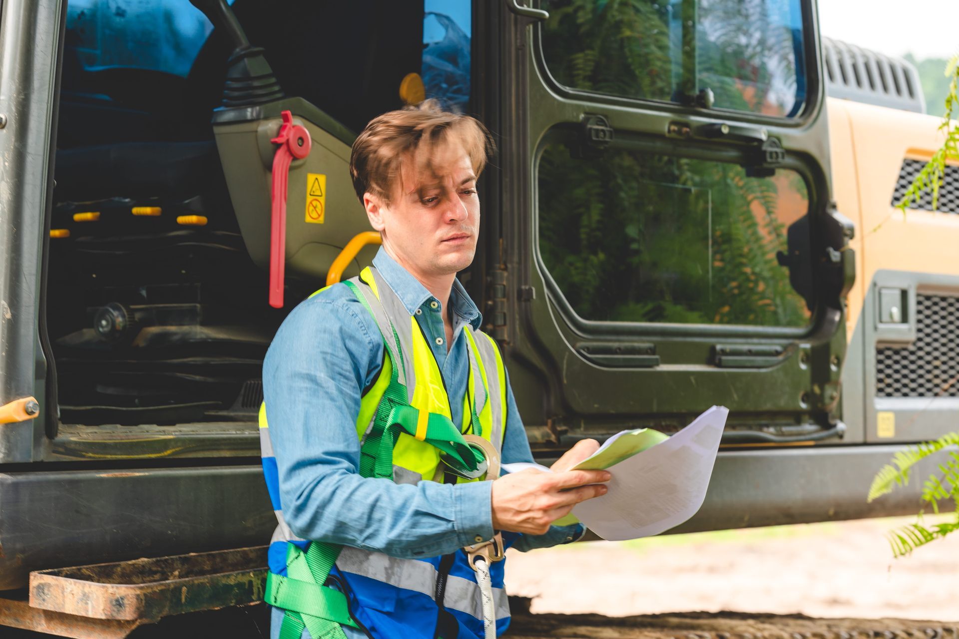 Worker in a safety vest holding papers beside a truck trailer outdoors