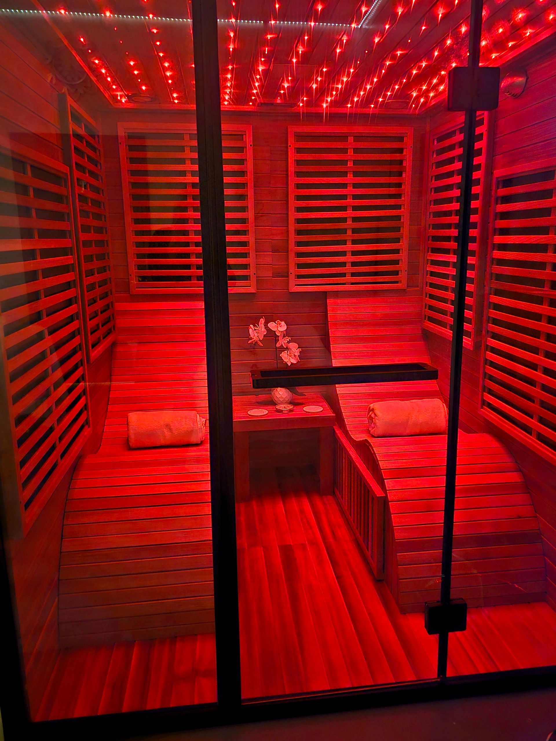 Red-lit sauna or spa room with wooden benches, slatted walls, and a small center table